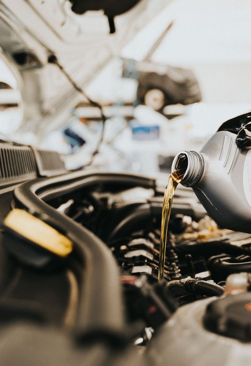 Close-up of a mechanic pouring engine oil into a car engine in an auto repair shop.