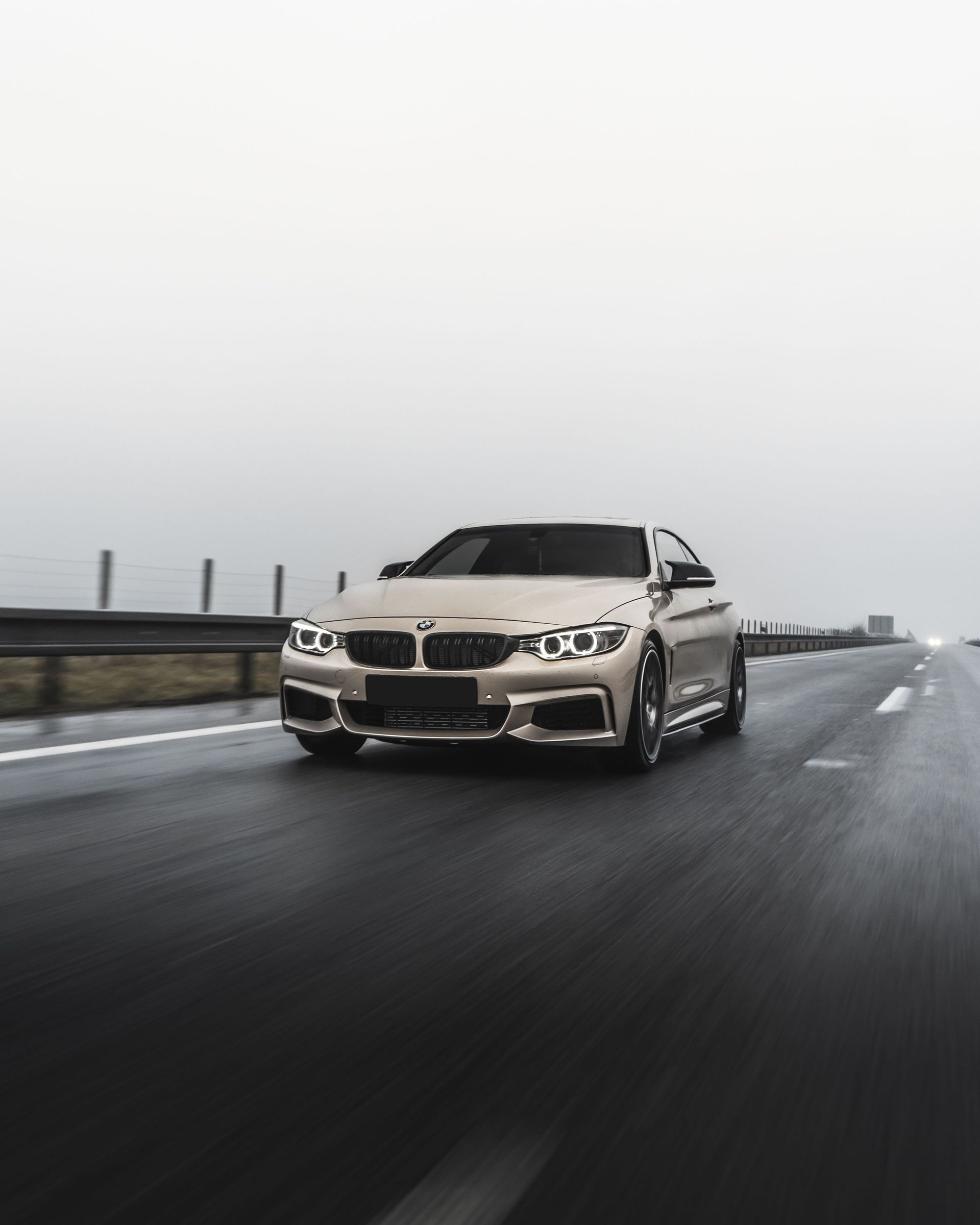 Sleek BMW car driving on a wet road with foggy weather, capturing speed and style.