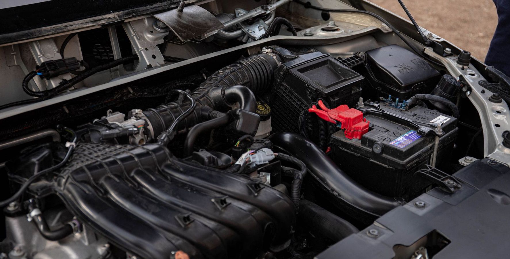 Mechanic inspecting car engine bay and battery during routine maintenance.